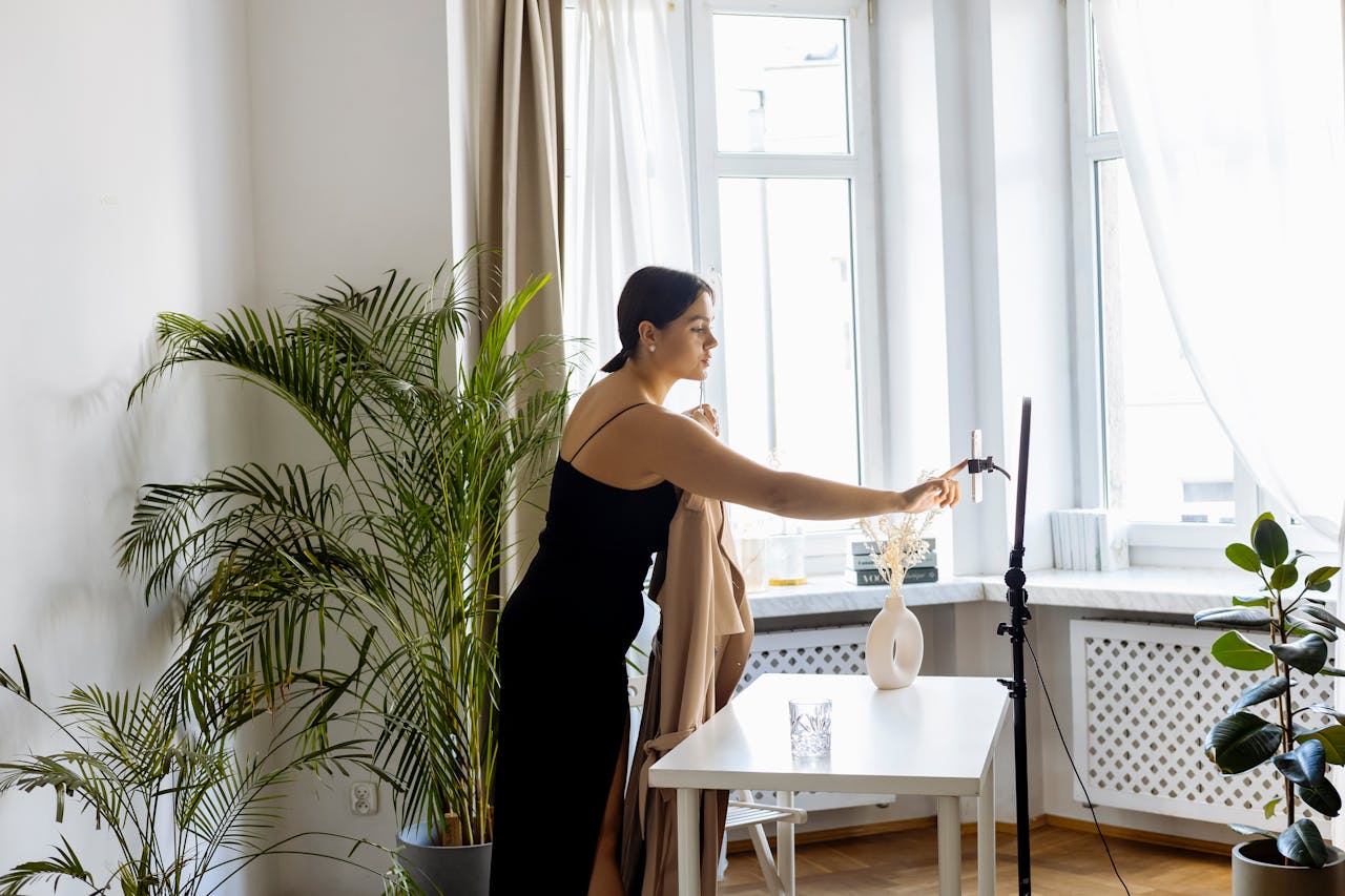 Businesswoman vlogging indoors using a smartphone setup, surrounded by plants and natural light.
